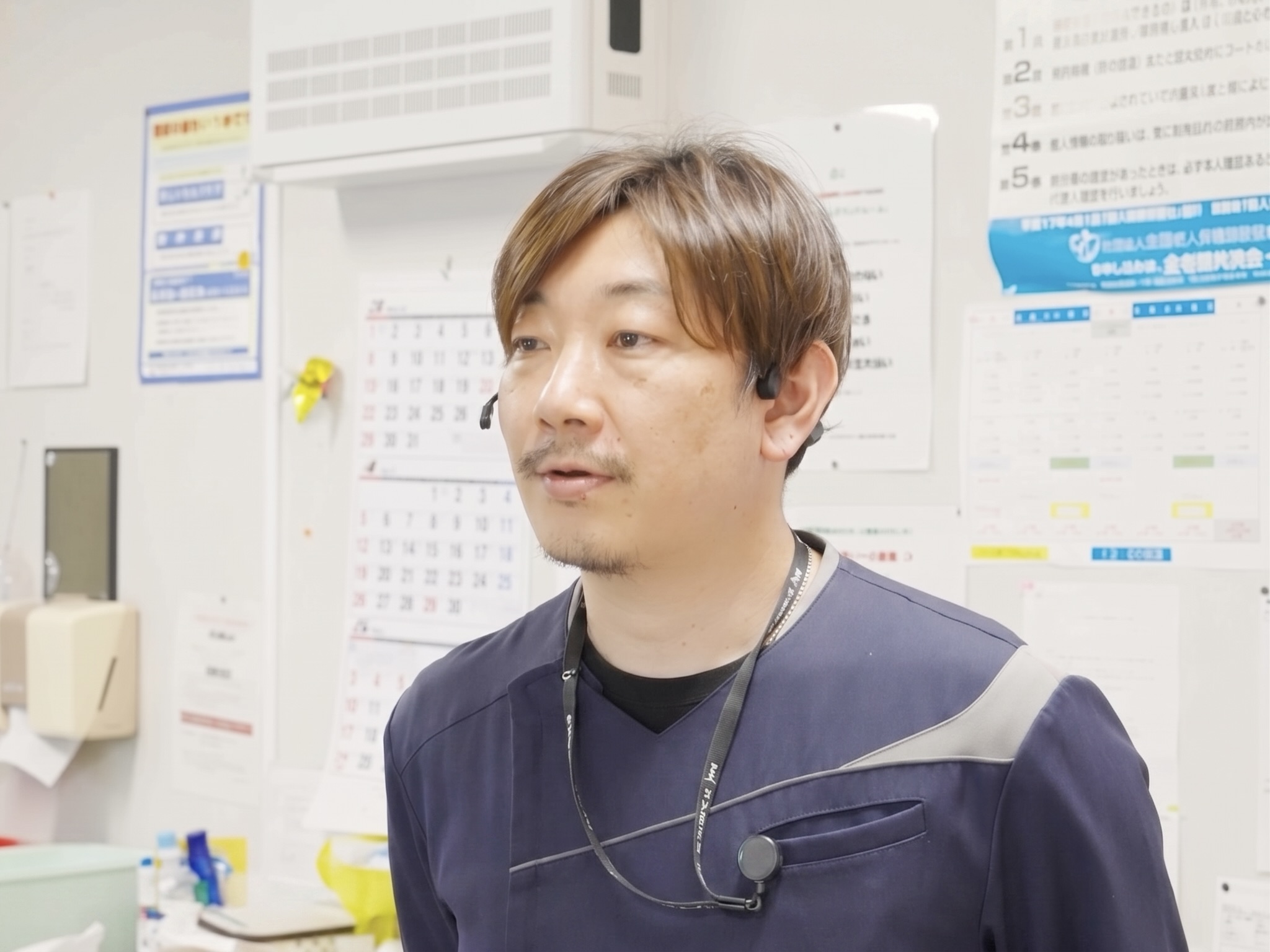 あさひホーム OpenComm2 PTTを着用しインタビューに応じる男性看護師のイメージ
