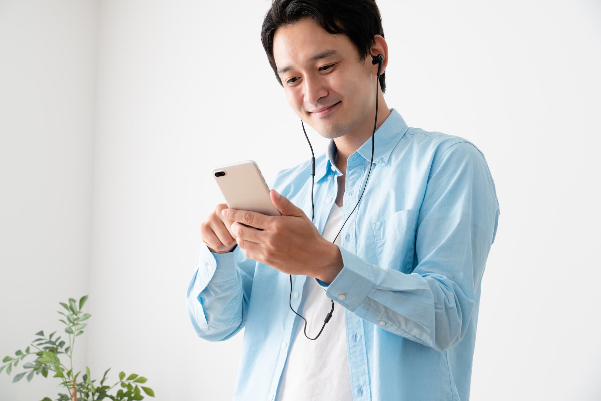 スマホに有線マイク付きイヤフォンを接続している男性のイメージ